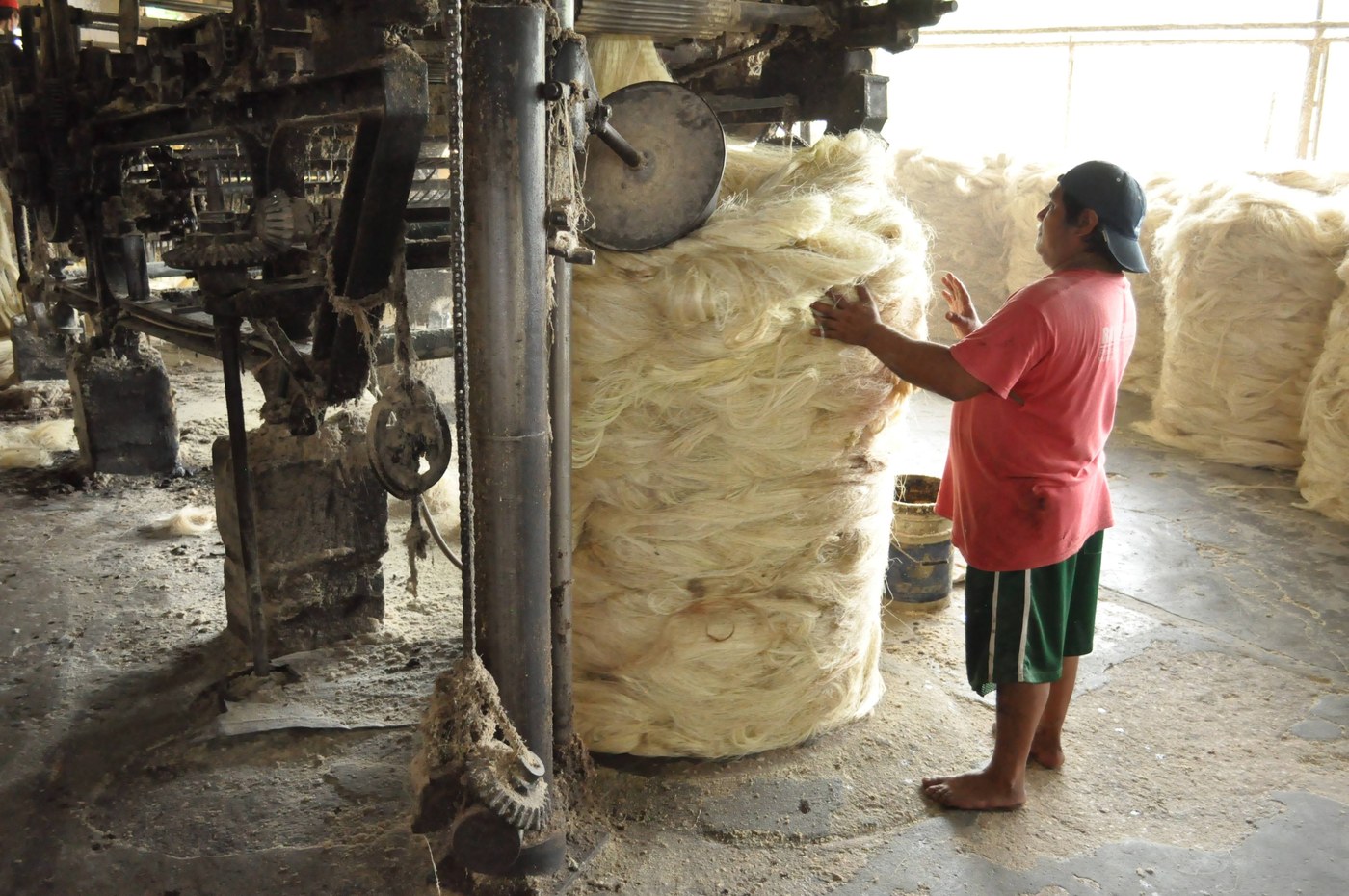 A worker in a textile plant handling raw fiber bundles beside machinery.