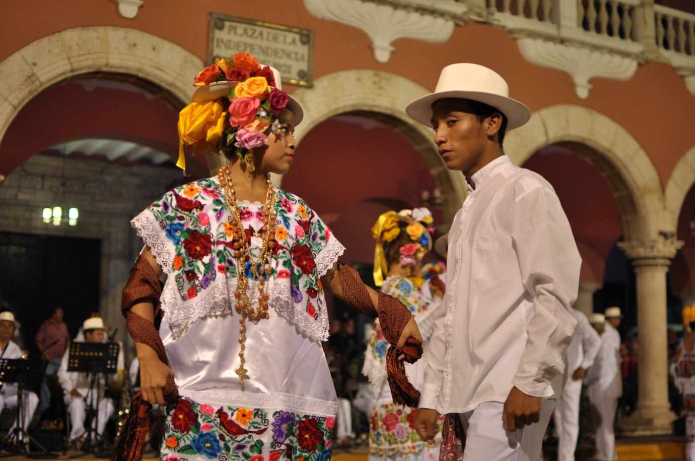 A couple in traditional festival attire standing beneath arched colonial architecture.